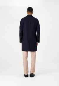 Cabană de marină cu o croială ajustată, mâneci lungi și un design dreapt. Asortată cu pantaloni bej deschis și pantofi negri.