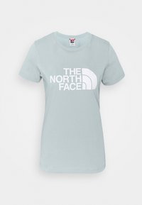 Světle modré bavlněné tričko s krátkým rukávem, které na přední straně nese velké bílé logo s nápisem "THE NORTH FACE".
