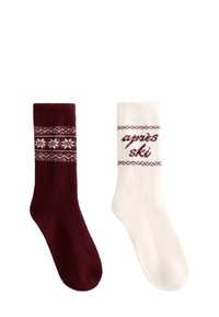 Para wełnianych skarpetek, jedna ciemnoczerwona z białym wzorem śnieżynek, druga biała z czerwonym wzorem i napisem "après ski", zimowy styl.