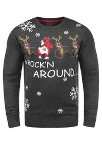 Pull en tricot gris foncé avec rennes rouges et bruns, flocons de neige, et texte "ROCK'N AROUND..." en blanc. Conception classique à col rond.