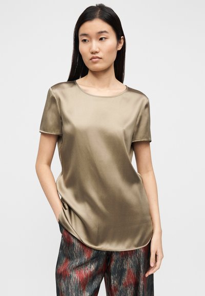 Κοντομάνικο ελαιίσιο σατέν τοπ με στρογγυλή λαιμόκοψη και άνετη εφαρμογή, συνδυασμένο με σκουρόχρωμο παντελόνι με σχέδια σε αποχρώσεις κόκκινου και γκρι.