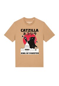 Tan katoenen t-shirt met een grafisch ontwerp van een zwarte kat voor een rode zonsondergang en een wit gebouw, met de teksten "CATZILLA" en "KING OF PAWSTER."