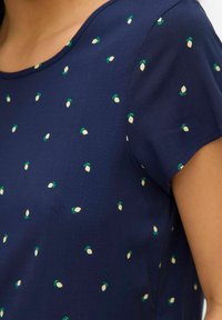 Marineblauwe blouse met korte mouwen, met een verspreid patroon van witte en groene bladvormen op een gladde stof. Ronde halslijn.