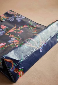 Transparante blauwe tas met een bloemenpatroon met roze vogels, paarse bloemen en groene takken. Gladde textuur met gestikte randen.
