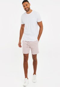 T-shirt bianca a collo rotondo abbinata a pantaloni corti rosa chiaro. I pantaloni corti hanno un elastico in vita e sono indossati con sneakers bianche. Texture del tessuto liscia.