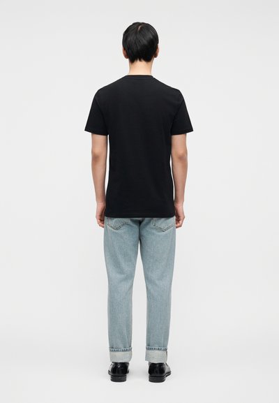 Μαύρο βαμβακερό μπλουζάκι με στρογγυλή λαιμόκοψη, κοντά μανίκια και άνετη εφαρμογή, συνδυασμένο με ανοιχτόχρωμο μπλε τζιν και μαύρα παπούτσια.