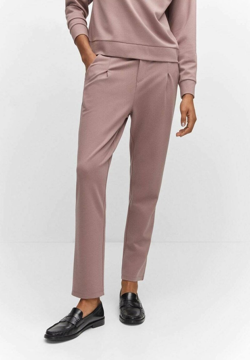 Pantalones rosa claro con un corte ajustado, que incluyen bolsillos delanteros y detalles de pliegues, combinados con mocasines negros. Textura de tela suave.