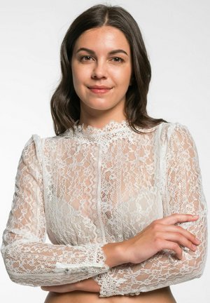 White lace blouse with long sleeves, high neckline, intricate patterns, and pearl button accents on the cuffs. Sheer texture throughout.