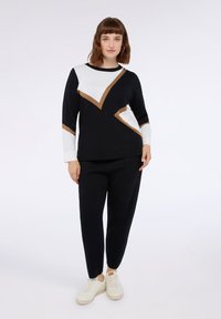 Czarny sweter z geometrycznymi białymi i beżowymi wzorami, okrągły dekolt. W zestawie z czarnymi wąskimi spodniami i białymi sneakersami. Miękka dzianinowa faktura.