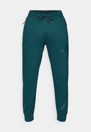 Blågrønne sweatpants med elastisk talje, snor og tapered ben. Har sidelommer med lynlås og diskret logo detalje på låret.