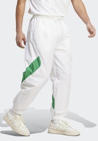 Bijele trenerice s zelenim bočnim naglascima, elastičnim pojasom i manžetama; izrađene od glatkog, laganog materijala; u paru s bijelim tenisicama.