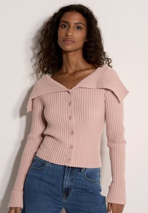 Rosenfarbener gerippter Cardigan mit weitem Kragen und Knopfleiste. Lange Ärmel mit ausgestellten Manschetten. Jeans aus Denim unterhalb der Taille zu sehen.