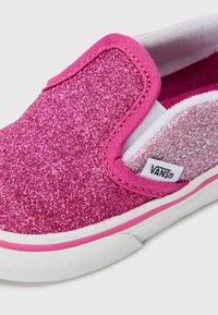 Chaussure rose pailletée à enfiler avec une doublure intérieure blanche, dotée d'une semelle en caoutchouc rose et d'un accent argenté subtil sur un côté. Étiquette de marque visible.