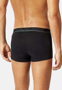 Boxer-briefs noirs en tissu lisse avec une ceinture élastique douce portant le nom de la marque "uncover" en gris.