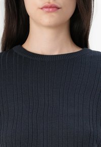 Mørkstripet genser med rund hals, med et teksturert strikkemønster. Stoffet virker mykt og har en tettsittende design.