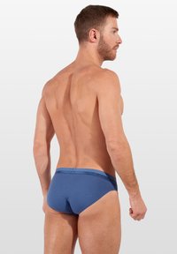 Modré pánské boxerky vyrobené z měkké tkaniny, s logem na pásku a těsným střihem. Jednoduchý design bez viditelných vzorů nebo akcentů.