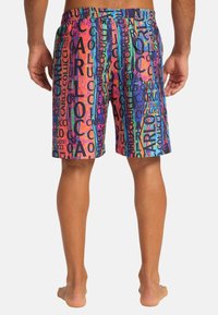Colorful swim shorts featuring an all-over pattern of the name "Carlo Colucci" in various colors, elastic waistband, and knee-length cut.