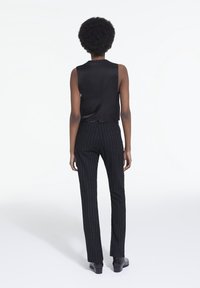 Top sans manches en satin noir associé à un pantalon à rayures verticales. Coupe ajustée, texture lisse et longueur aux chevilles. Bottines noires.