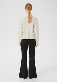 Světlé šedé, texturované, zkrácené svetr s klesajícími rameny spárovaný s černými, rozšířenými kalhotami. Pohled zezadu, ukazující celý outfit.