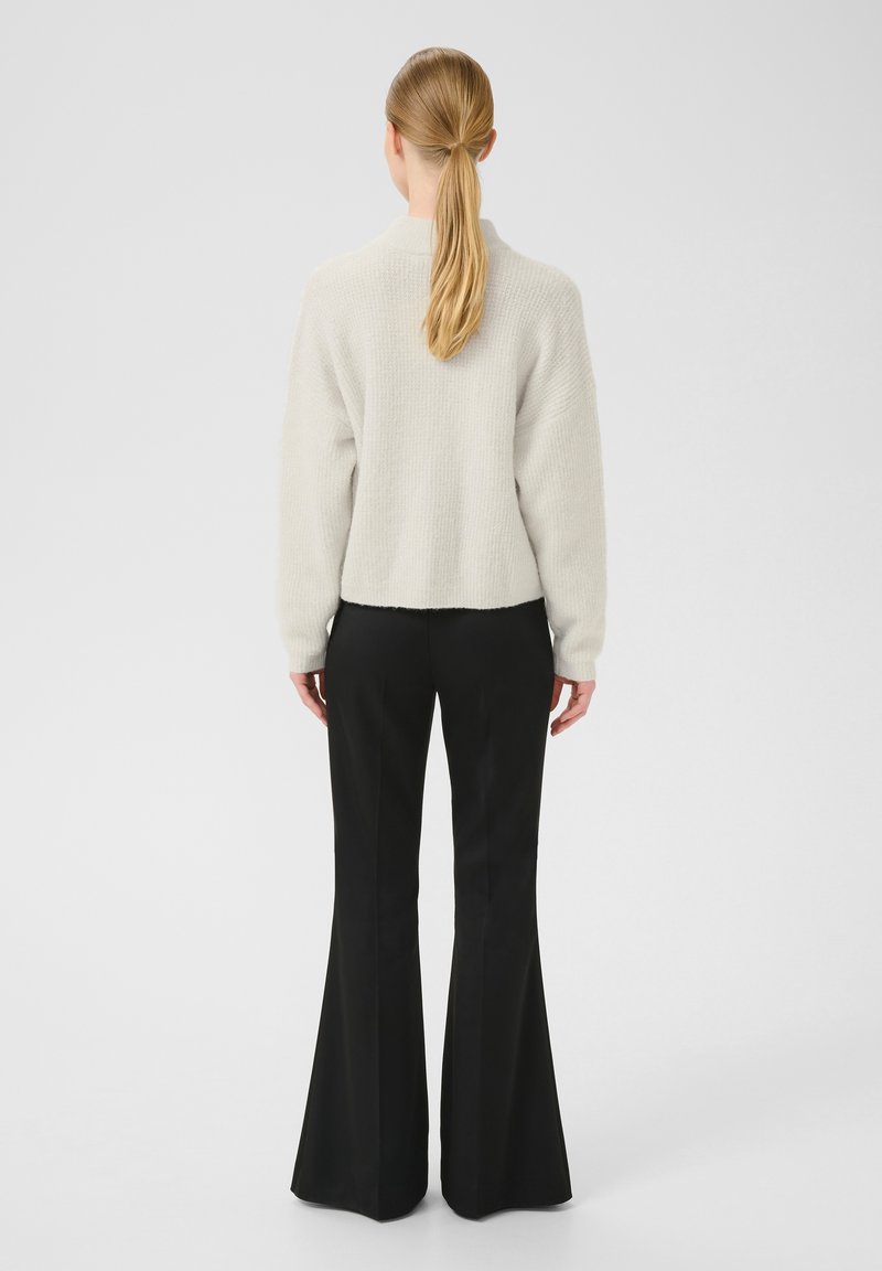 Pull court en gris clair texturé avec des épaules tombantes, associé à un pantalon noir évasé. Vue de dos, montrant l'ensemble de la tenue.