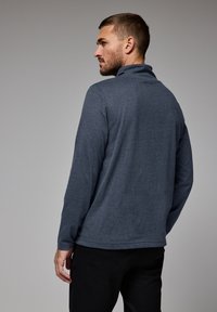 Pullover gris oscuro de manga larga con cuello ligeramente levantado, fabricado en un tejido suave; textura lisa con costuras mínimas y sin patrones visibles.