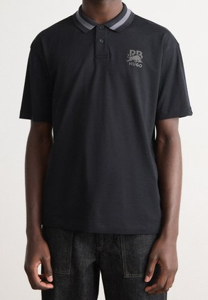 Black polo shirt with grey-striped collar, featuring a small embroidered logo on the left chest. Soft, breathable fabric; short sleeves.