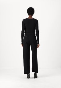 Zwarte geribbelde lange-mouwen top gecombineerd met hoge taille zwarte broek. De outfit wordt aangevuld met zwarte hakken, die een getailleerd silhouet hebben.