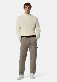 Maglione a collo alto a coste color crema abbinato a pantaloni cargo grigi. L'outfit presenta una cintura nera e sneakers bianche, il tutto in una palette di colori neutri.