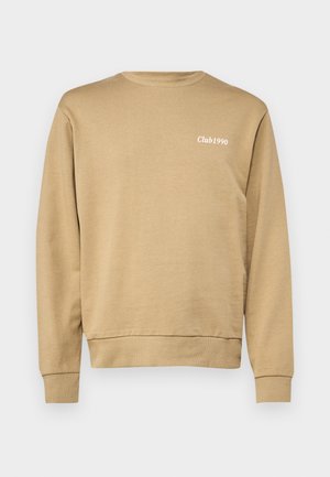Sweatshirt beige avec col rond et poignets côtelés, arborant un discret texte "Club1990" en blanc sur la zone du côté gauche de la poitrine. Texturé lisse.