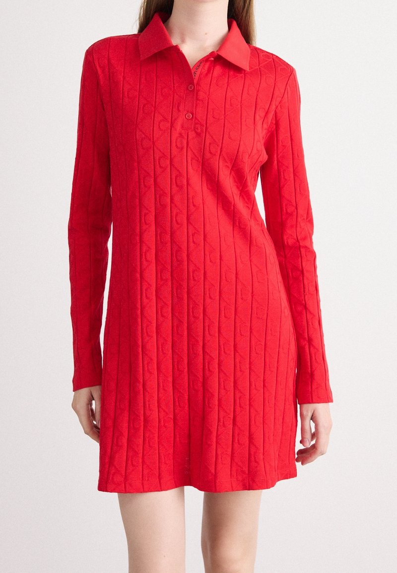 Femme portant une mini-robe rouge à manches longues en tricot avec un col et trois boutons à l'avant.