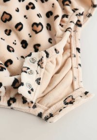 Fluffy beige bodysuit with black leopard and heart patterns. Three metallic snaps at the bottom for easy dressing. Soft texture.
