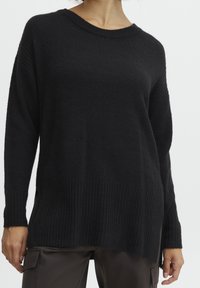 Czarny sweter dzianinowy o luźnym kroju, z ribbowanym dołem i długimi rękawami. Miękka tekstura i szeroki dekolt dodają mu wyjątkowego charakteru.