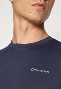 Sötétkék t-shirt sima anyagból, kerek nyakkivágással, bal mellkason fehér "Calvin Klein" logóval.