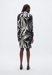 Svart-hvitt marmorert mønstret kjole med lange ermer, tettsittende silhuett og knelengde hem. Glatt stoff og enkel kragedetalj.