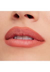 Nærbilde av lepper med en matt ferskenrosa farge, som viser en jevn tekstur og definert form. Tennene er hvite og synlige.