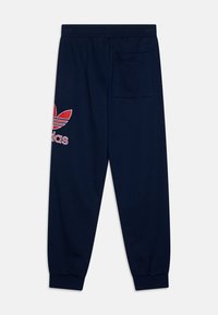 Calças de fato de treino azul marinho feitas de algodão, apresentando o logotipo vermelho da Adidas, bolso lateral e cintura elástica com punhos. Design clássico afunilado.