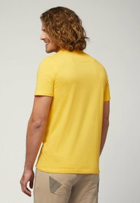 T-shirt giallo a maniche corte con scollatura rotonda. Texture liscia, vestibilità casual, indossato con pantaloni beige chiaro con dettagli a contrasto.