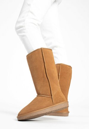 Tan suede knee-high boots with a rounded toe, simple stitching, and a textured rubber sole. The upper features a soft finish.