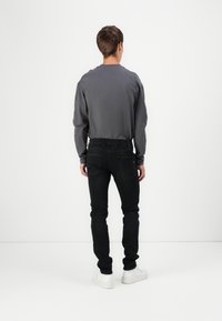 Šedá košile s dlouhým rukávem, černé slim-fit džíny a bílé tenisky. Jednoduchý design, měkká textura, se standardními umístěními zadních kapes.