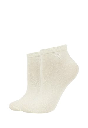 Coppia di calzini beige alla caviglia con bordi a coste e un piccolo logo ricamato vicino alla parte superiore su sfondo bianco.