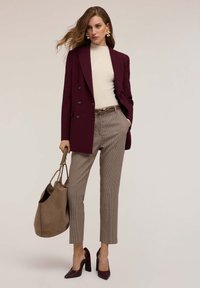 Bordeaux dubbelzijdig colbert gecombineerd met een crèmekleurige geribbelde trui, bruine geruite broeken en bordeauxhoge hakken. Inclusief een beige handtas.