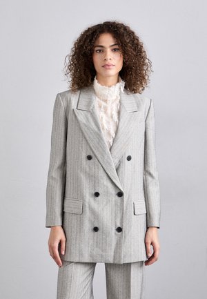 Grau gestreifter, doppelt geknöpfter Blazer mit schwarzen Knöpfen und seitlichen Taschen, über einer cremefarbenen, strukturierten Bluse getragen. Glatte Stoffoberfläche.