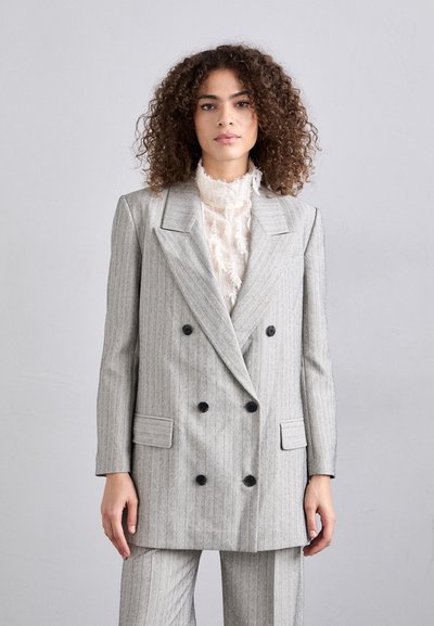 Blazer a doppio petto grigio a righe con bottoni neri e tasche laterali, indossato sopra una blusa crema texturizzata. Finitura del tessuto liscia.
