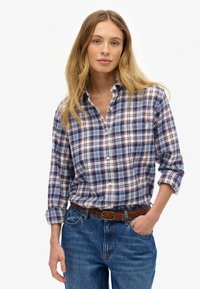 Katoenen geruite shirt in marineblauw, wit en bordeauxrood met een button-down kraag. Lange mouwen opgerold bij de manchetten. Draagt het met blauwe jeans en een gevlochten riem.