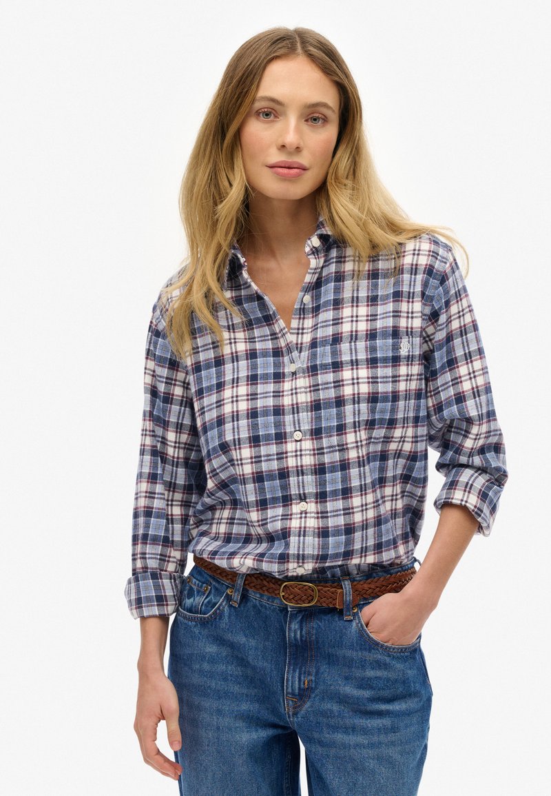 Katoenen geruite shirt in marineblauw, wit en bordeauxrood met een button-down kraag. Lange mouwen opgerold bij de manchetten. Draagt het met blauwe jeans en een gevlochten riem.