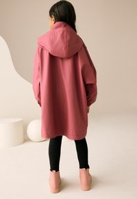 Rózsaszín vízálló dzseki kapucnival, bő szabású, elasztikus mandzsettákkal és kenguruzsebekkel, fekete leggingsszel és rózsaszín bokacsizmával párosítva.