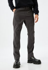 Pantalones gris oscuro, ajustados y con una textura suave, con parches en las rodillas. Combinados con botas negras gruesas, que tienen una cremallera en el tobillo.