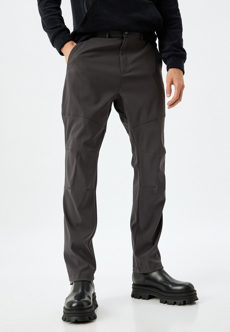 Pantalones gris oscuro, ajustados y con una textura suave, con parches en las rodillas. Combinados con botas negras gruesas, que tienen una cremallera en el tobillo.