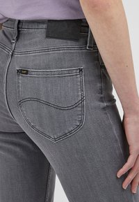 Grå denimjeans med en åtsittande design, prydda med bakfickor med en böjd söm och en liten varumärkesetikett. Slät textur och minimal hårdvara.
