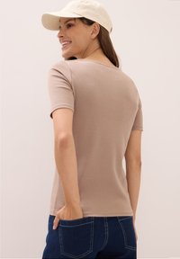 Béžové tričko s krátkým rukávem a kulatým výstřihem, měkkou texturou a přiléhavým střihem, kombinované s tmavě modrými džíny s viditelným švem.